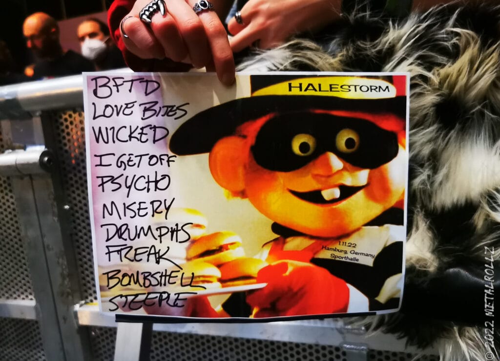 Setliste mit einer Comicfigure in gelb Orange und Augenbinde wie eine Verbrecher. Links stehjen hanschriftlich die Lieder untereinander.